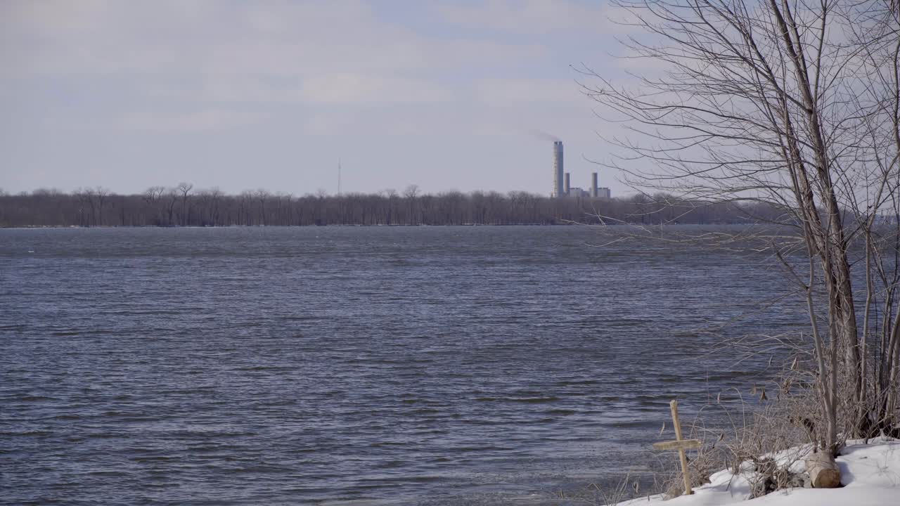 Waves flowing on the river by a grave and smokestack in winter