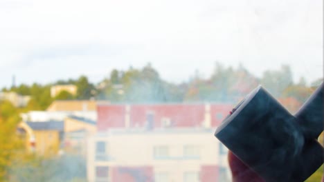 burning-up-quality-tobacco-filled-inside-a-modern-pipe-smoked-by-a-Caucasian-male-in-his-30s-wearing-a-red-shirt-and-long-ginger-beard-with-a-town-nature-houses-in-the-back-clouds-of-smoke