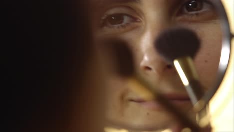 young woman putting on makeup with brush adding blush bronzer on her face