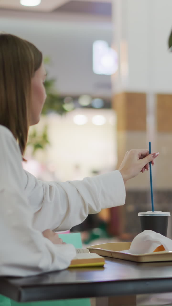 inserción de paja a mano en la taza de café colocada en una bandeja con papas fritas cubiertas en un entorno de comedor casual, el fondo incluye elementos borrosos del restaurante, sillas y vegetación