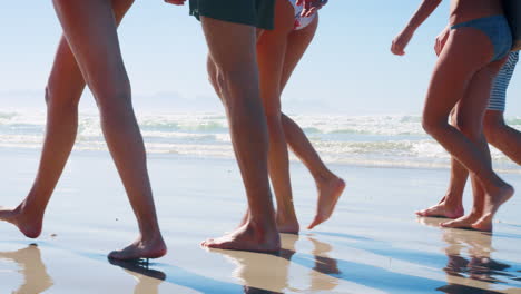 cerca de las piernas de los amigos caminando a lo largo de la costa en vacaciones en la playa