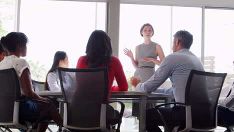 A-young-businesswoman-standing-speaks-at-a-meeting