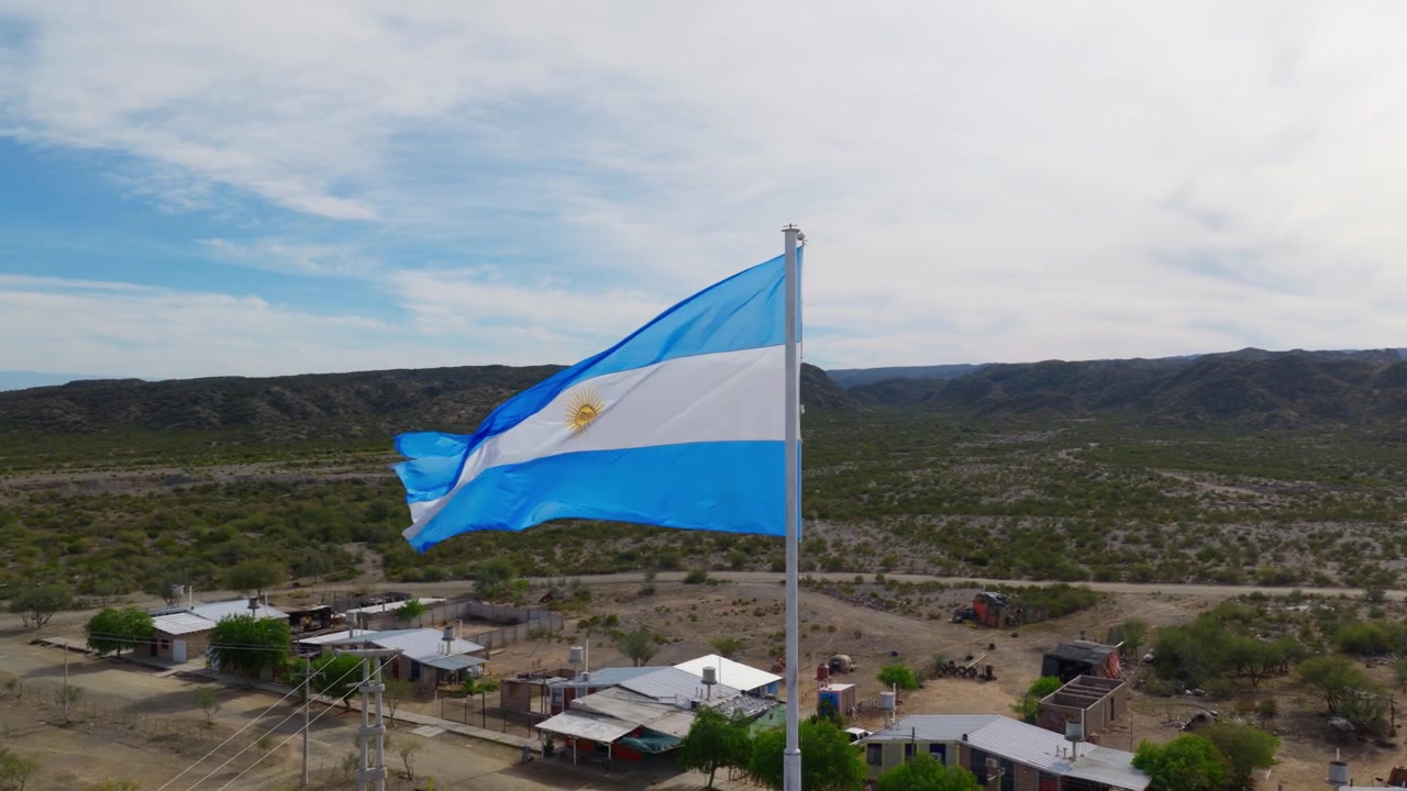 Prise de vue par drone en cercle rapproché autour d'un grand drapeau argentin sur un mât en ville.