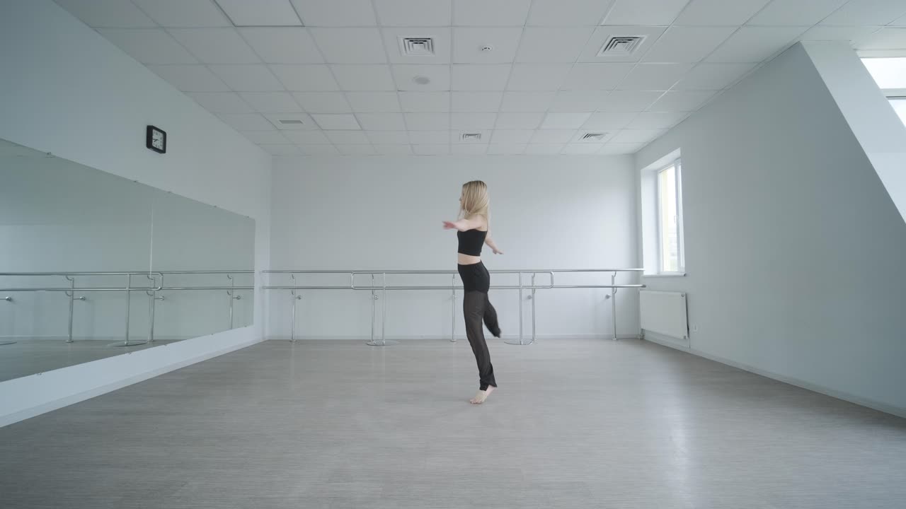 Trænet pige i sort tøj udfører moderne dans. Kvindelig danser viser flydende bevægelser, krop og hænder bølger i et hvidt rum. Moderne balletkoreografi. Ung kvinde bevæger sig smidigt