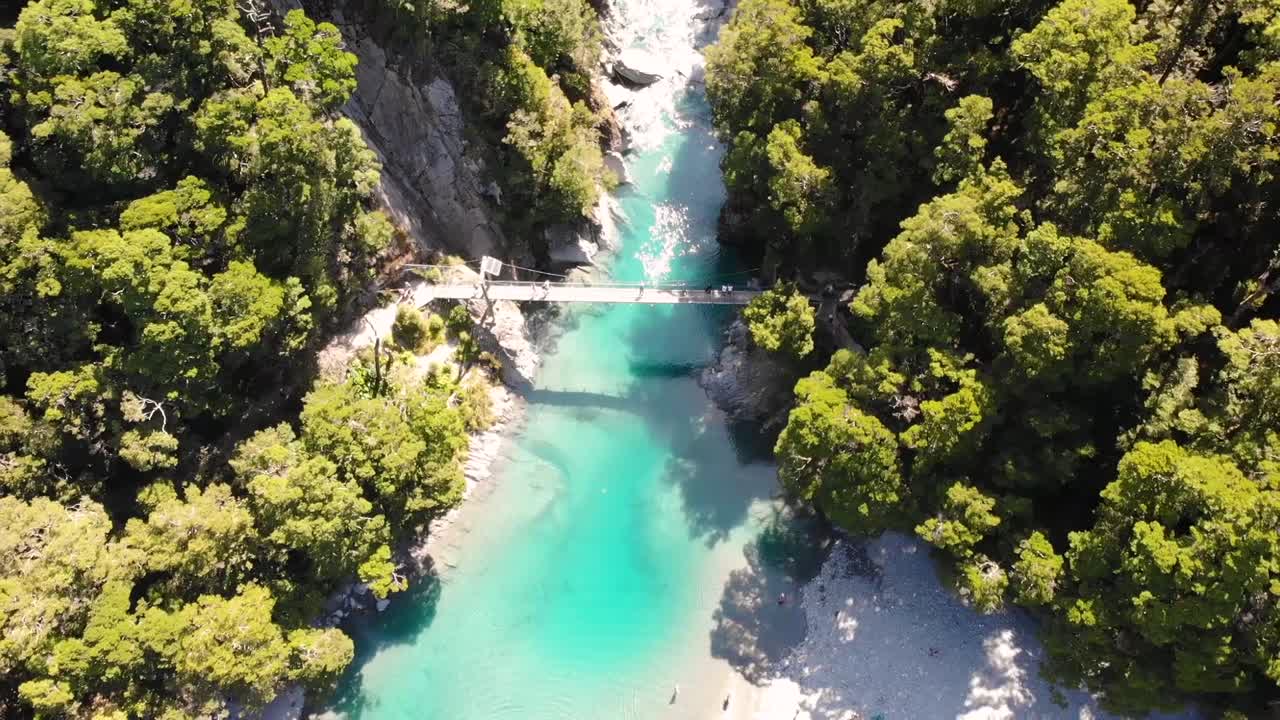 puente oscilante sobre el desfiladero del río azul en piscinas azules rodeadas por el exuberante bosque en un día soleado en la isla sur de nueva zelanda