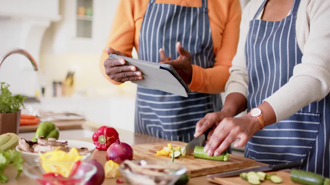 pareja de ancianos afroamericanos preparando una comida usando una tableta en la cocina, cámara lenta