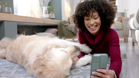 Happy-biracial-woman-with-golden-retriever-dog-using-smartphone-at-home,-slow-motion