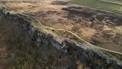 Dramatic-aerial-footage-circling-beautiful-rock-formation-with-colourful-terrain-and-a-long-open-trail