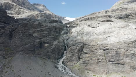 avión no tripulado volando hacia una pequeña cascada hecha de agua derretida glacial que baja de una montaña rocosa