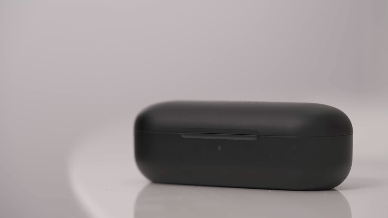 Sorte trådløse hovedtelefoner isoleret på hvid baggrund. Mandlig hånd lægger trådløse øretelefoner i opladningsetuiet.