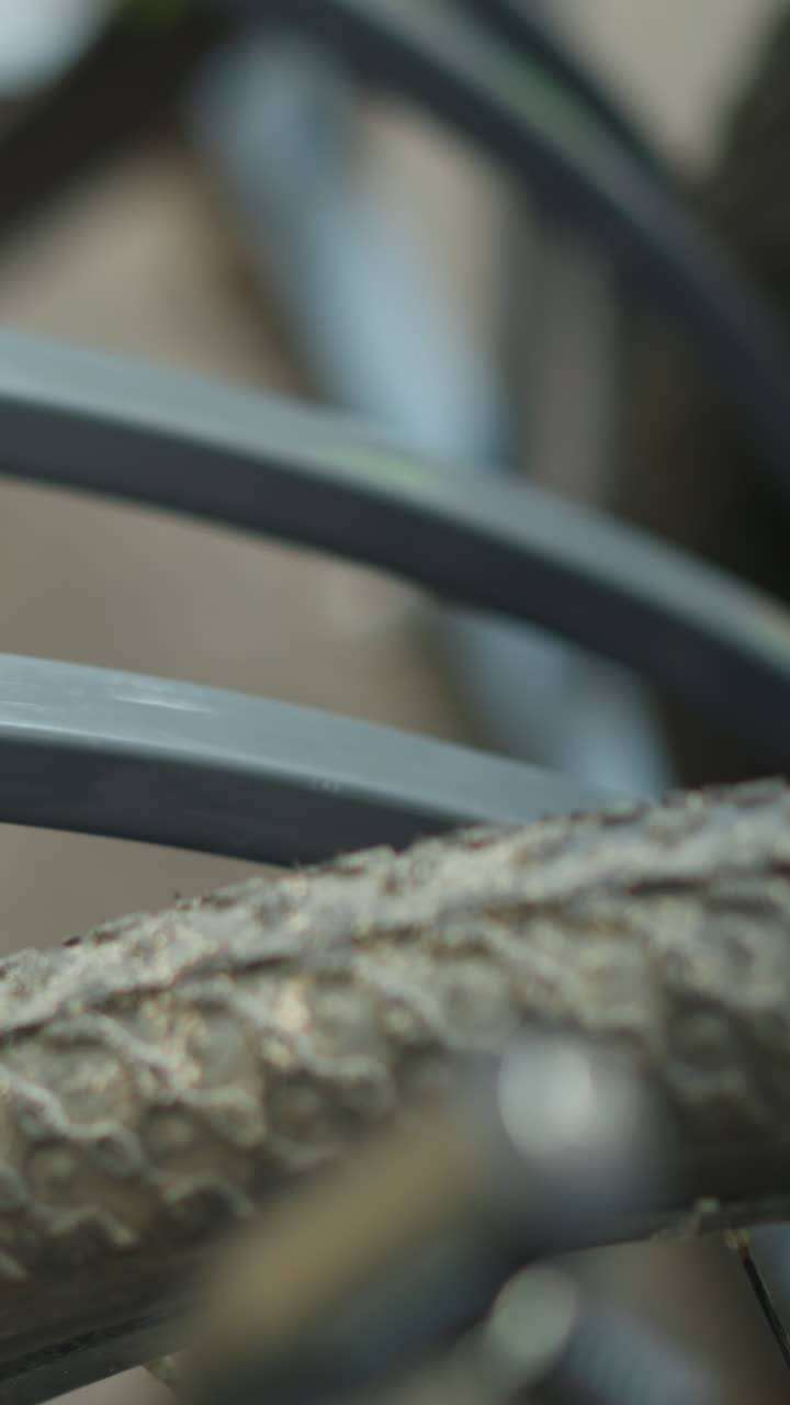 primer plano de un neumático de bicicleta asegurado en un soporte de bicicleta de metal con enfoque en la rueda texturizada y el marco de metal, el fondo muestra otra bicicleta borrosa estacionada cerca