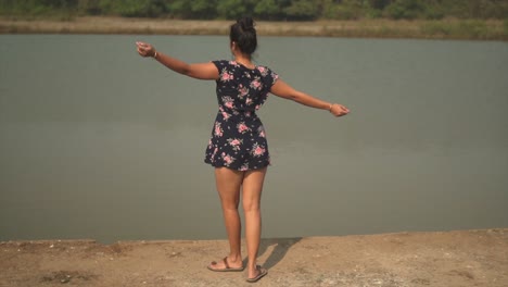 young brunette girl on a raised area next to a place with water feeling free by her gestures