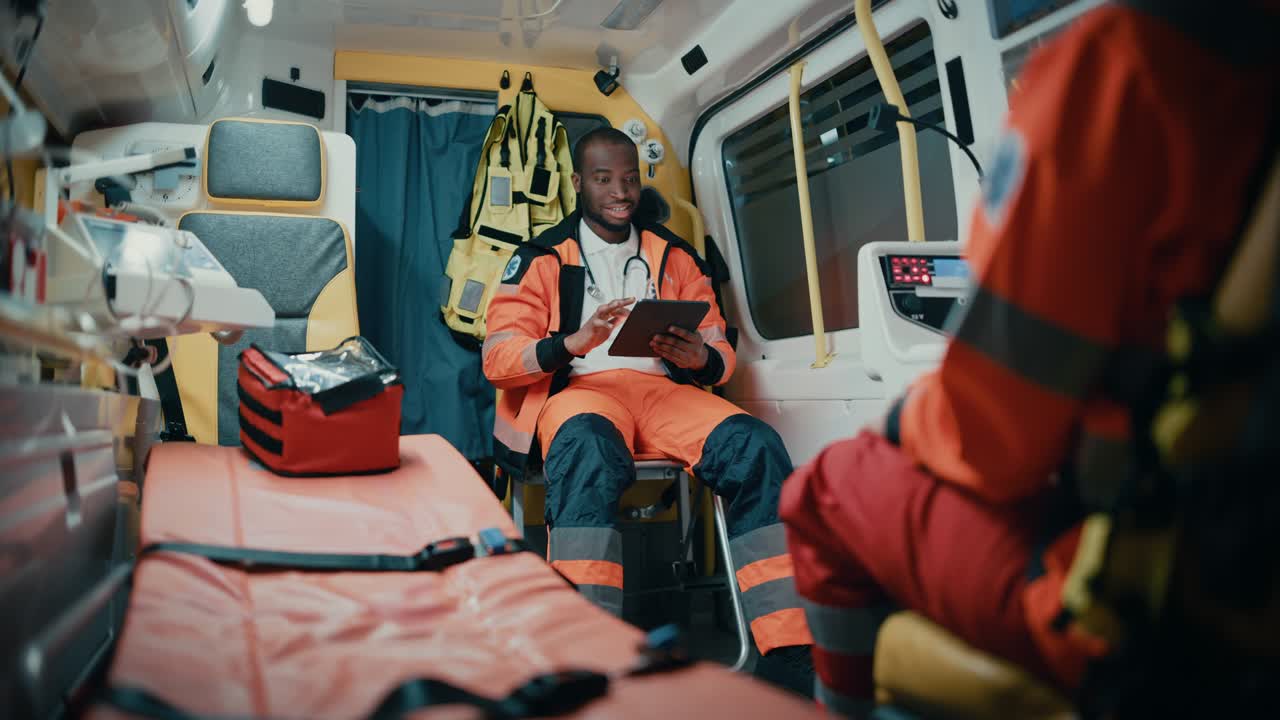 아프리카계 미국인 구급대원들이 응급차를 타고  컴퓨터를 사용하면서 응급 의료 기술자들이 의료 병원 밖에서 호출을 받고 있습니다.