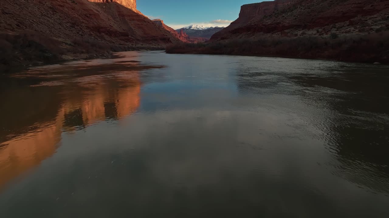 Dramatic canyon landscape at dusk with golden cliffs and glowing sky mirrored on still water, aerial dolly
