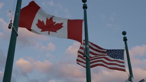 banderas estadounidenses y canadienses en astas de bandera que vuelan contra el cielo del atardecer en magog, quebec, canadá