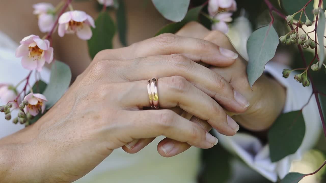 Tangan bergeser setelah genggaman lembut di taman closeup menunjukkan cincin emas, kuncup merah muda eukaliptus.