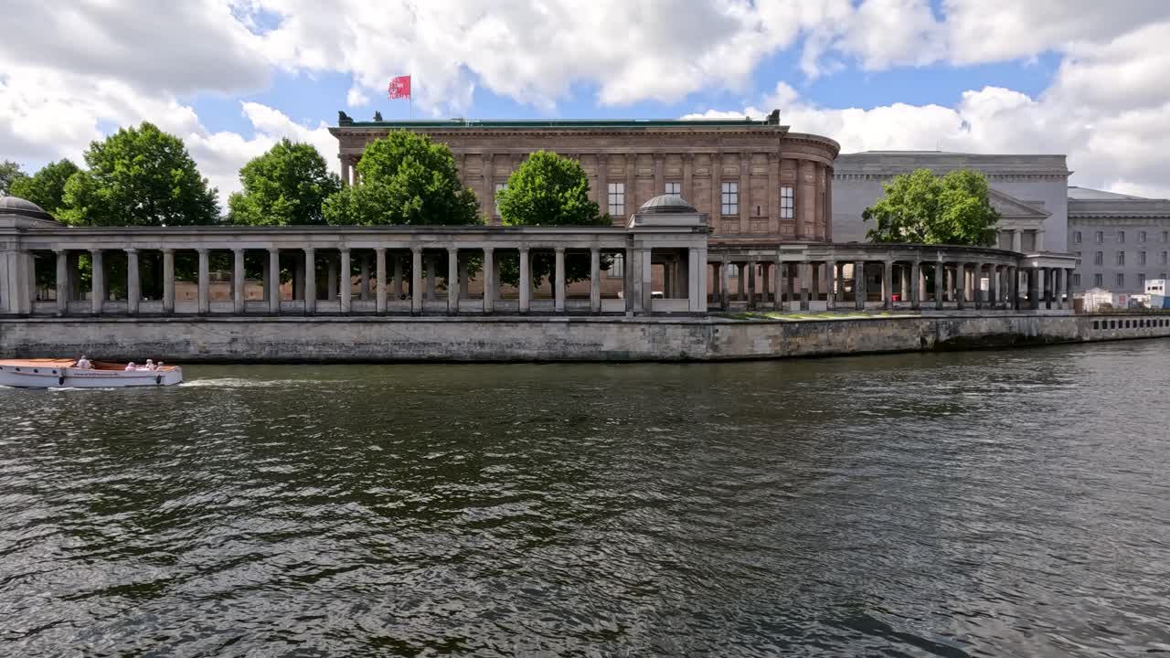 Tour boat cruises on river past historic neoclassical museum in Berlin under bright summer daylight