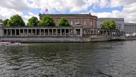 tour boat cruises on river past historic neoclassical museum in berlin under bright summer daylight