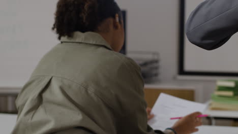 students in a classroom receiving papers from teacher