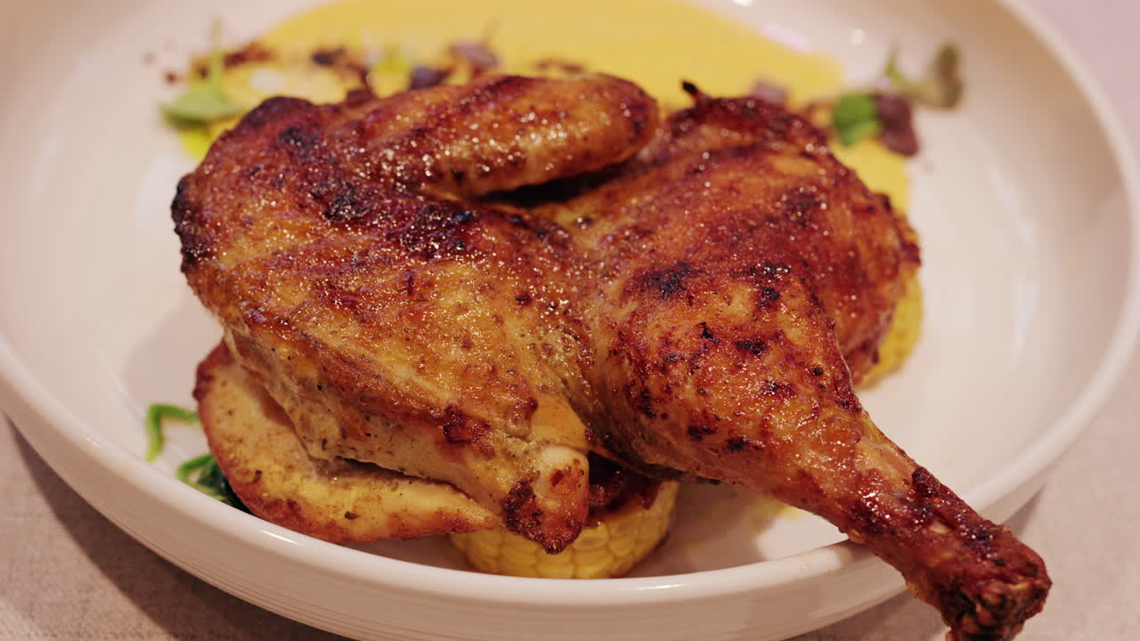 Primo piano di una coscia di pollo alla griglia servita con salsa cremosa, mais e verdure.