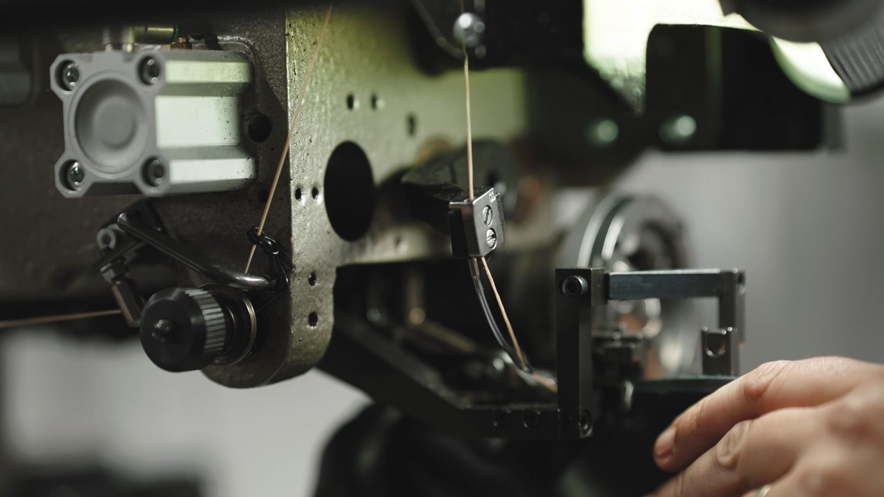 Technician adjusts thread guide on heavy industrial textile machine mechanism