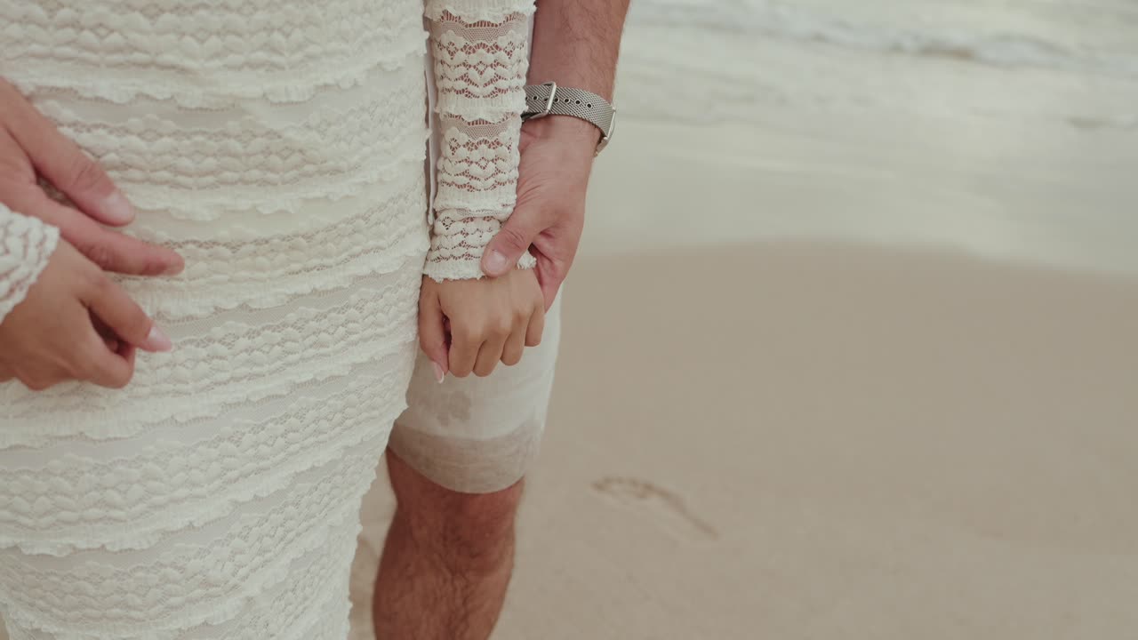 bride and groom hold hands on sandy beach by gentle ocean waves
