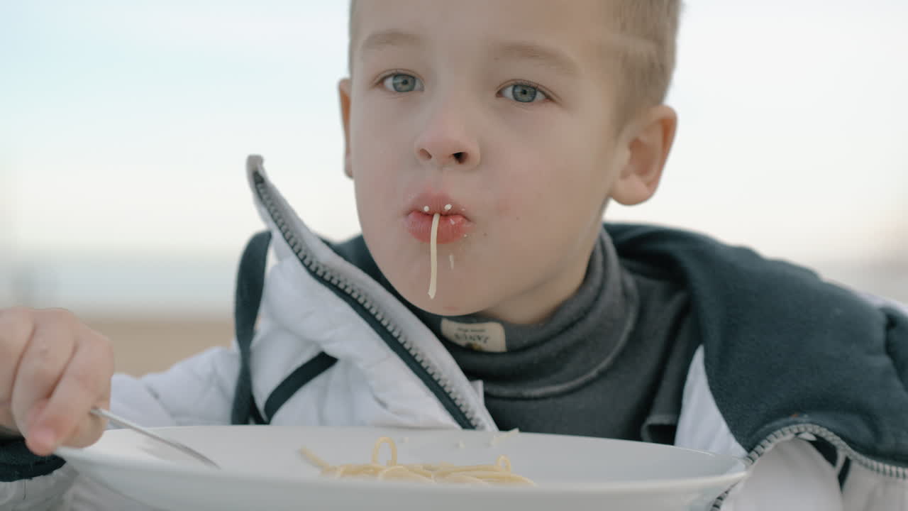 un niño comiendo pasta afuera.