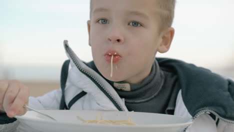 young boy eating pasta outside