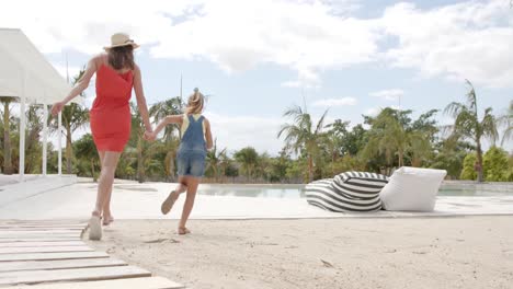 Kaukasische-Mutter-Mit-Tochter,-Die-Am-Strandhaus-Rennt-Und-Händchen-Hält