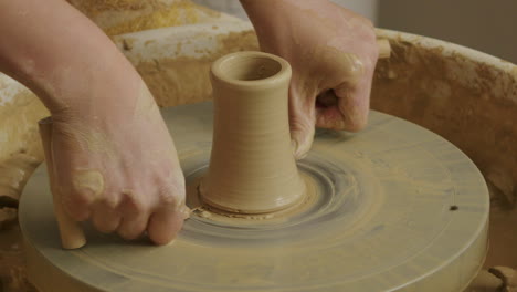 handheld close up shot of using a string to remove a wet clay vase from a potter's wheel for further steps