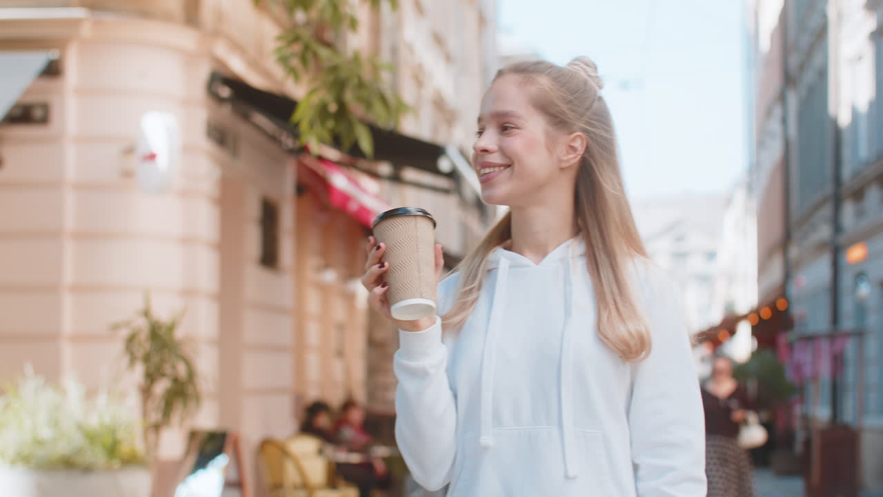 joven blanca feliz disfrutando de beber café de la mañana bebida caliente y sonriendo en la calle de la ciudad
