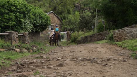 los africanos trotan caballos en un camino rocoso pasando por una casa de piedra en el pueblo de lesotho