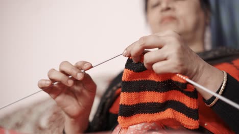mujer india tradicional mirando cómo tejer y continúa tejiendo con hilo negro y rojo