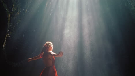 mujer feliz bailando en la cueva de la cascada salpicando agua usando un hermoso vestido disfrutando de la naturaleza bailando sintiendo libertad espiritual 4k