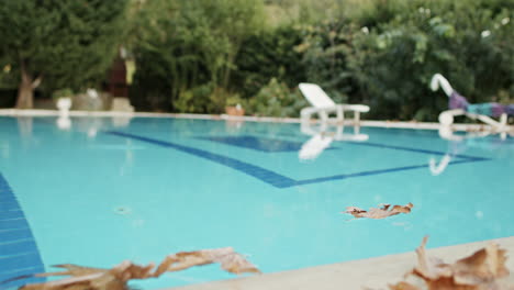 Wide-Shot-of-Fallen-Orange-Dried-Leaf-Wandering-on-top-of-Clear-Blue-Water-in-Swimming-Pool-with-Blowing-Wind-in-slowmo