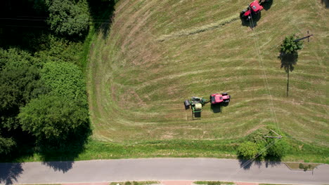 aerial view looking down at pair of diesel tractors gathering and forming bales on agricultural farmland