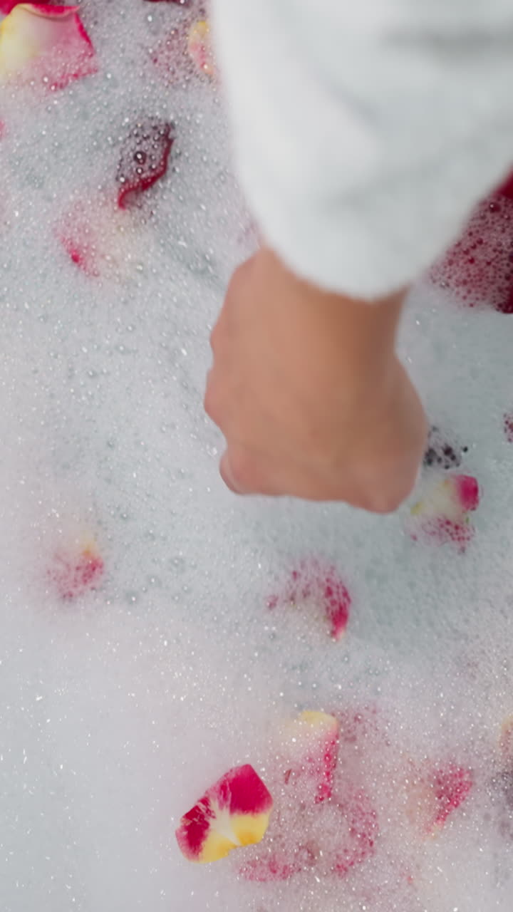 Woman touches foam with rose petals closeup. Lady prepares relaxation procedure in romantic atmosphere to celebrate Valentine day. Celebration idea