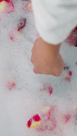 woman touches foam with rose petals closeup. lady prepares relaxation procedure in romantic atmosphere to celebrate valentine day. celebration idea