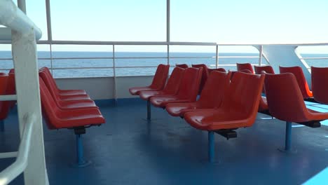 push in to red outdoor ferry seats in between railings with open sea in distance slow motion