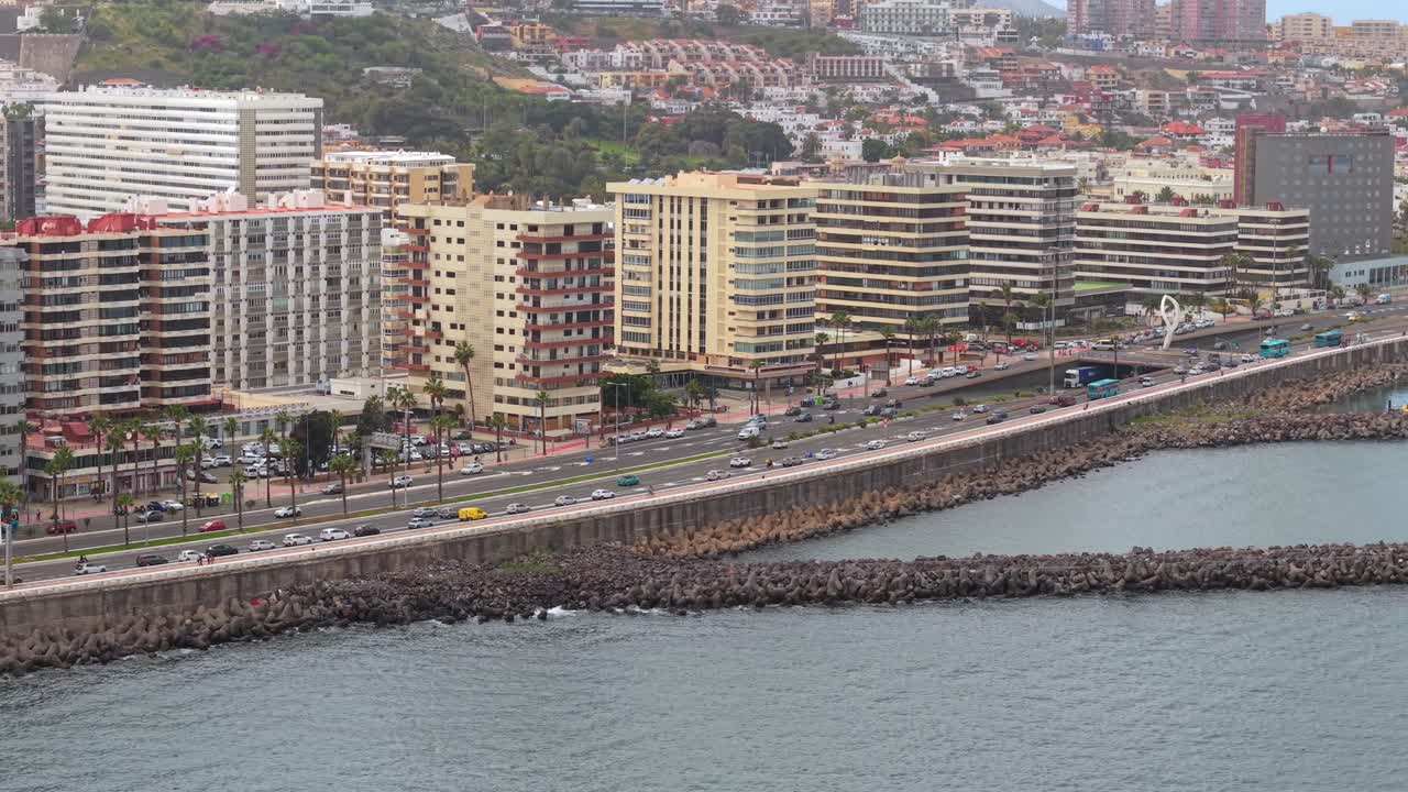 Vista aérea mostrando carros circulando na avenida costeira em Las Palmas de Gran Canaria, com edifícios modernos e o oceano