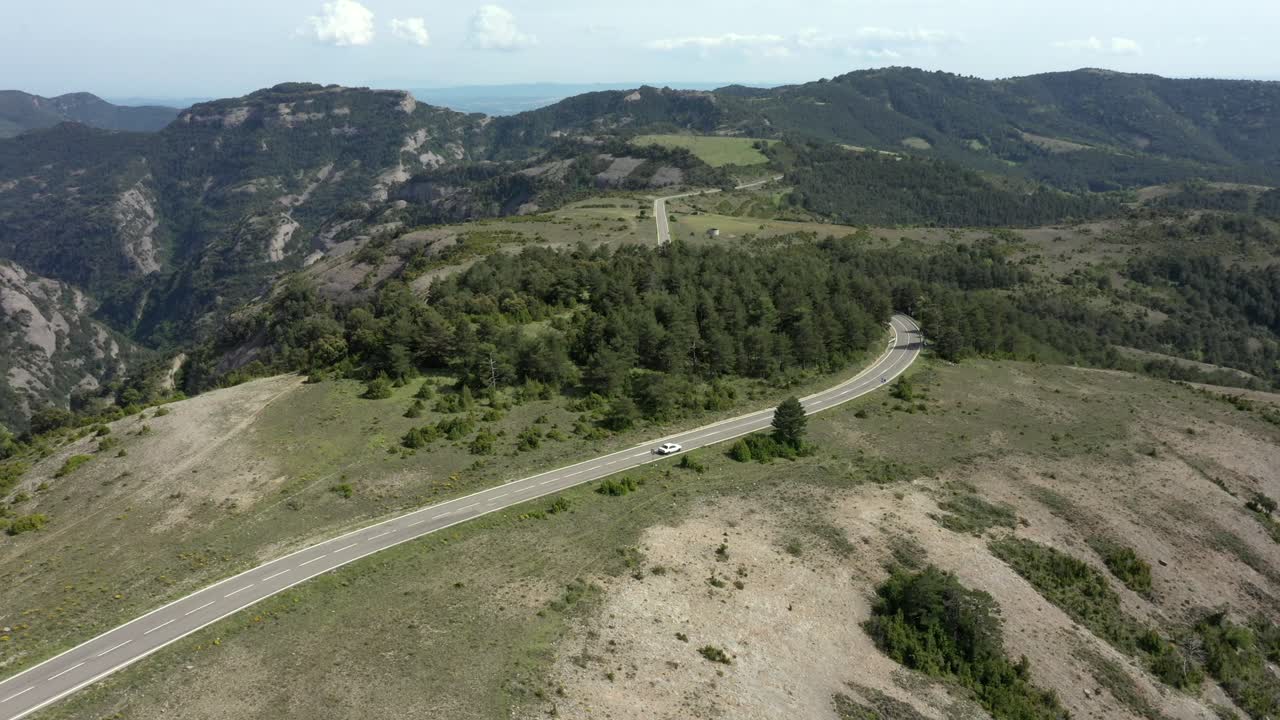 vista aérea de seguimiento de un pequeño coche blanco en una carretera de montaña vacía, tranquila y escénica, a lo lejos