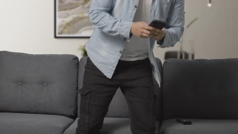 young man sitting on sofa at home with remote control flicking through tv channels