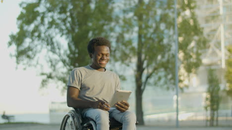 young guy in wheelchair having video chat on tablet in park