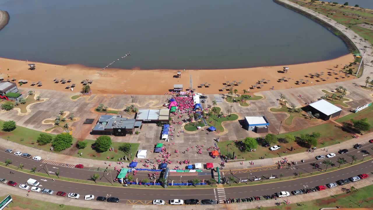 Vista aerea inclinata dall'alto verso il basso dei corridori della maratona Carrera Rosa in rosa riuniti per la cerimonia di premiazione vicino al traguardo, accanto al fiume e alla sabbia