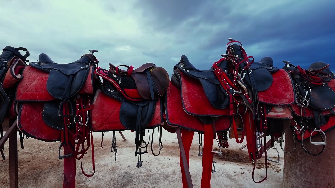 Fileira de selas de cavalo vermelhas em suporte de madeira sob um céu nublado dramático ao ar livre