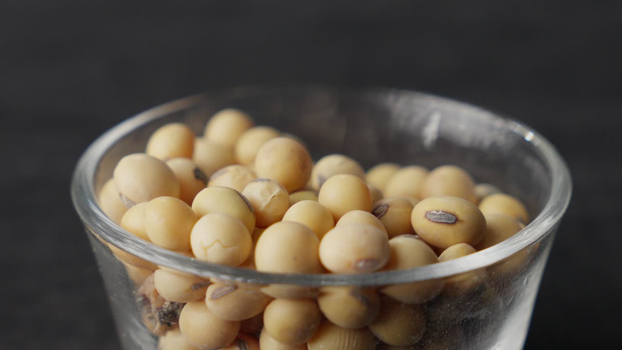 Soybeans falling from a spoon into a glass bowl in slow motion