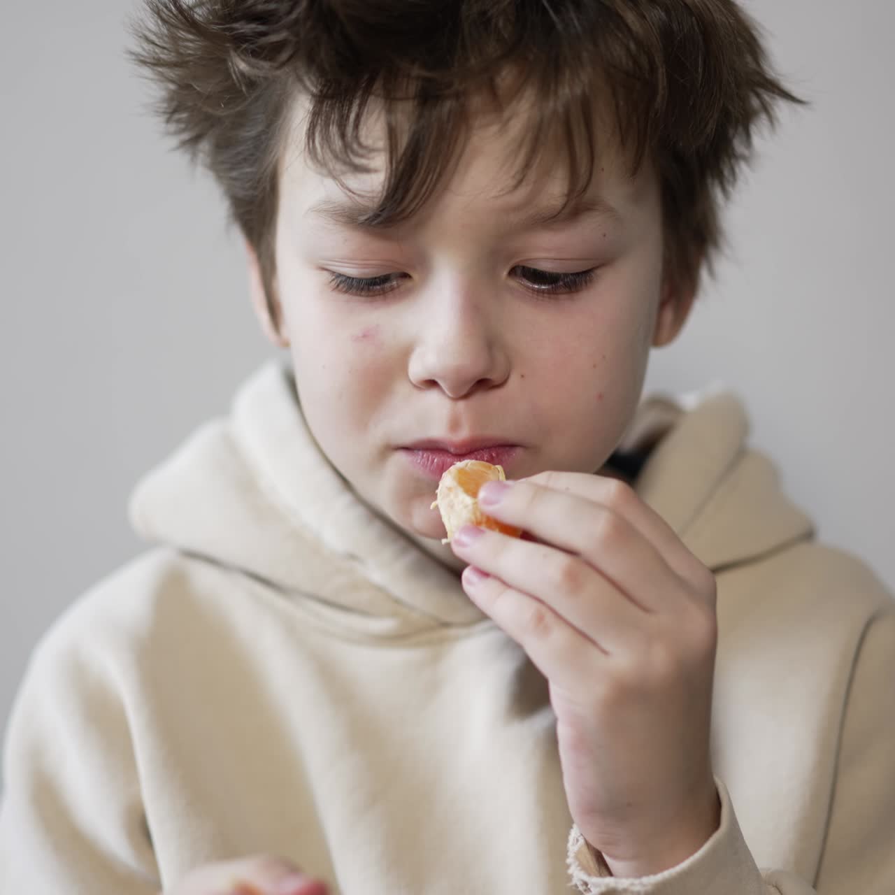 Teenager of thirteen years eating tangerine. The boy takes a piece by piece chewing a fruit. Close up