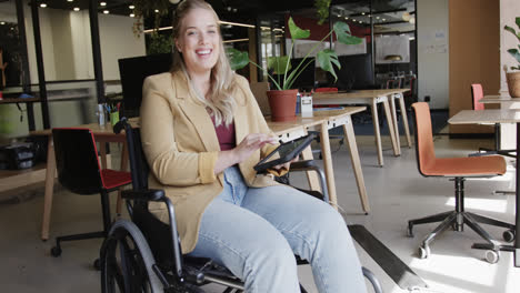 portrait of happy caucasian businesswoman in wheelchair using laptop in office, in slow motion