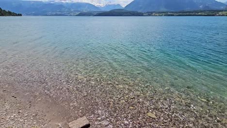 Static-shot-of-shore-of-lake-with-clear-water-and-mountains-in-background-in-Switzerland