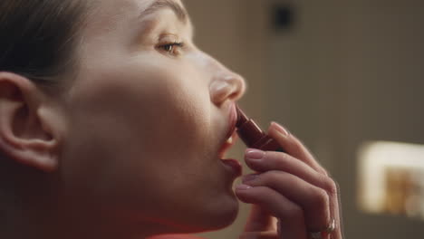 woman putting red gloss in lips closeup. party girl doing makeup in evening